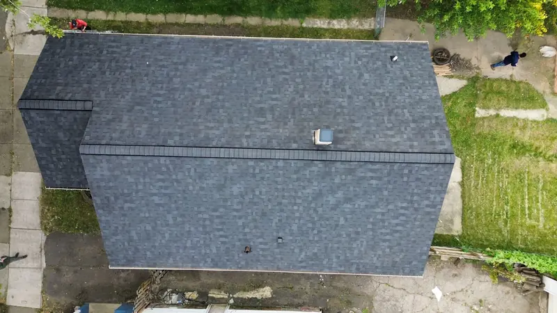 Straight-down drone view of a finished dark grey architectural shingle roof on a narrow house