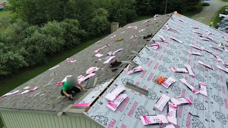 Large roof mid-replacement, with new synthetic underlayment covering half the roof and pink Duration shingle bundles staged across it